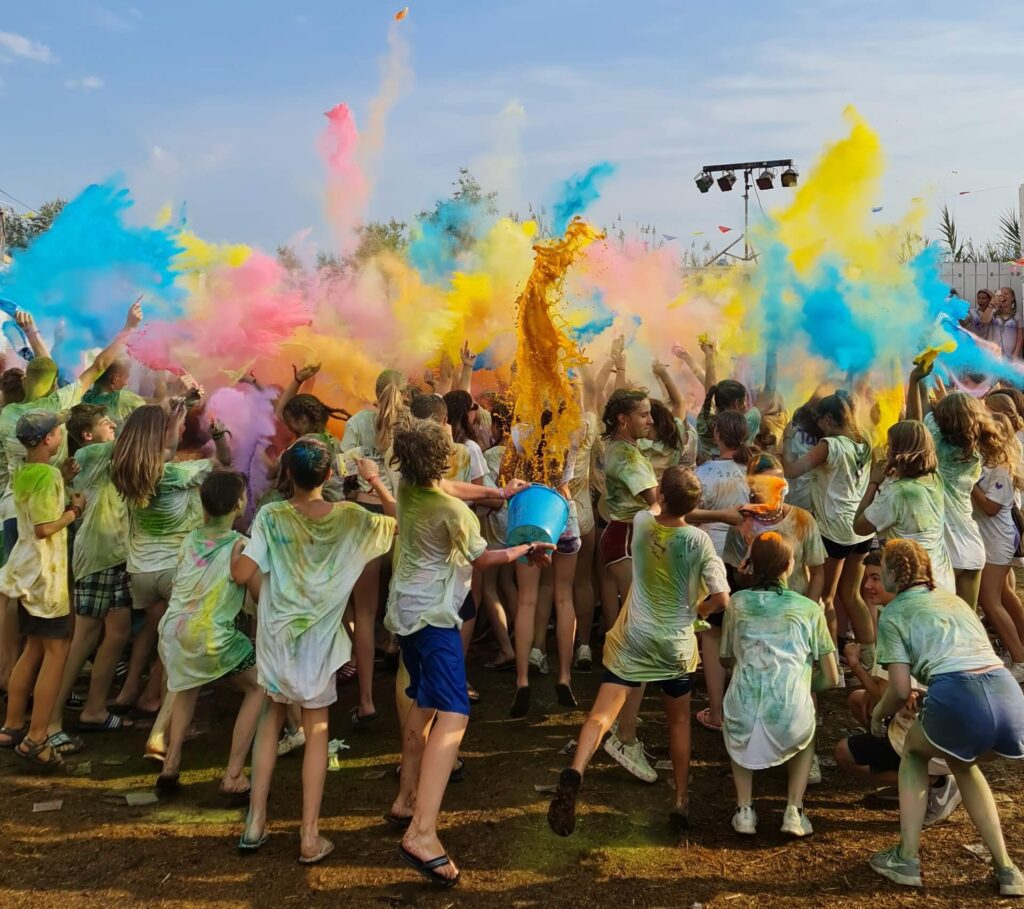 Jugendliche werfen bei einem Ferienlager Holifestival bunte Farbpulver in die Luft; fröhliche Stimmung und gemeinsames Erleben im Sommer-Camp von Wildfang e.V.