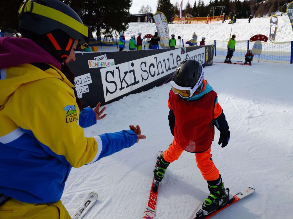 Kind im Skikurs beim Wildfang e.V. Ferienlager mit Betreuer*in im Hintergrund – Lernaktion im Kinderland Skischule, Winterferienbetreuung und Ferienlager-Teamer im Einsatz
