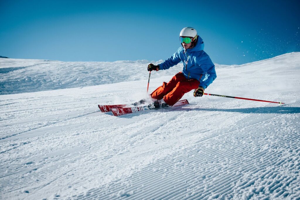 Skifahrer in blauer Jacke und Helm fährt dynamisch eine sonnige, präparierte Skipiste in den Alpen hinab – Wintersport, Ferienlager Jugendfreizeit, Kinder- und Jugendreise im Schnee
