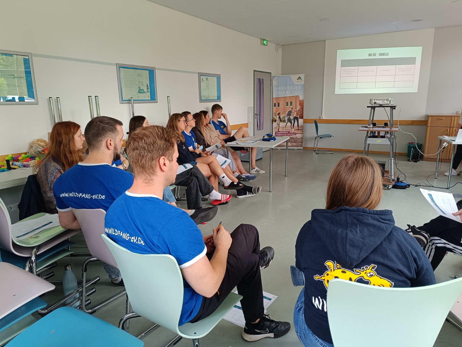 Campleiter sitzen im Halbkreis in einem Seminarraum und nehmen an einer Schulung für Ferienfreizeiten teil