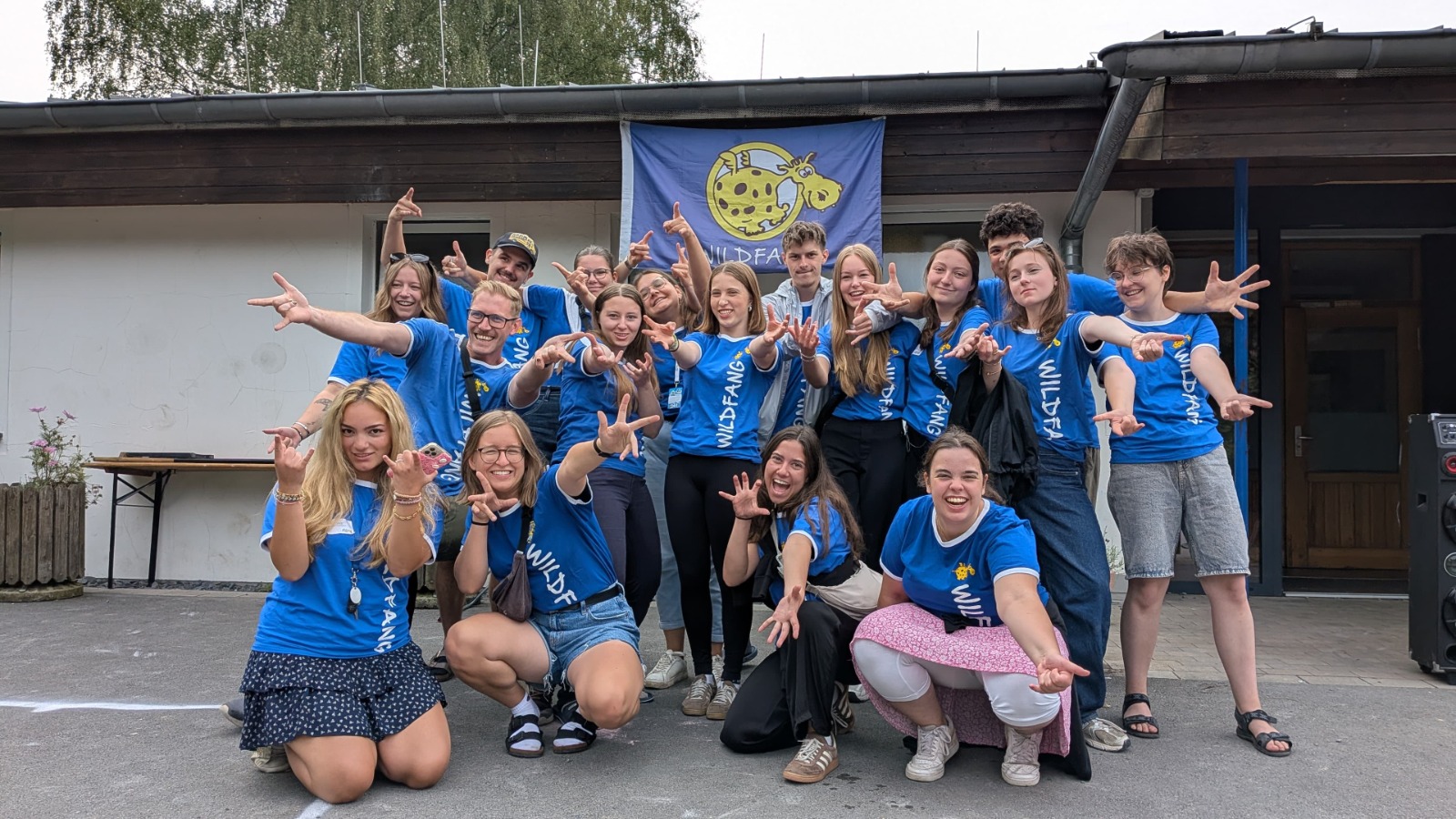 Junge Wildfang-Teamer in blauen T-Shirts stehen zusammen und strecken zum Abschluss des Sommercamps die Arme in die Höhe.