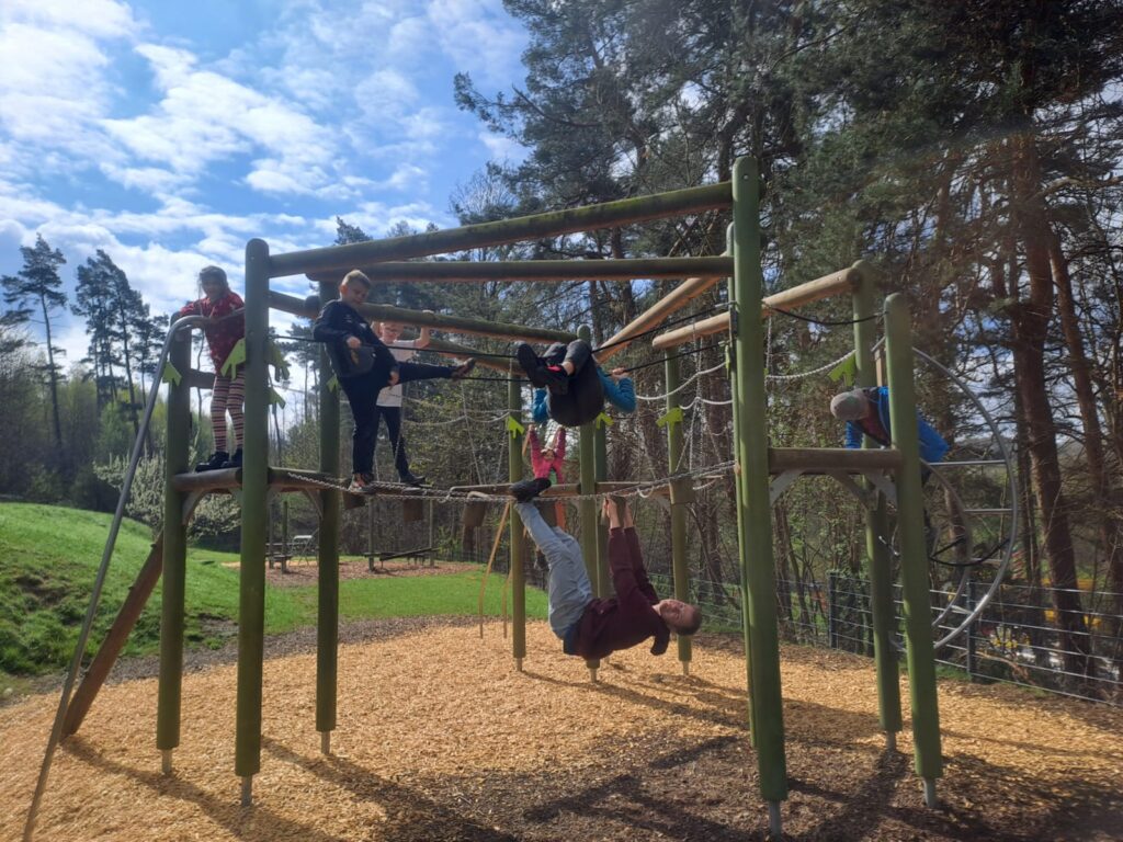 Kinder klettern gemeinsam mit einem Betreuer auf einem Klettergerüst während einer Ferienfreizeit